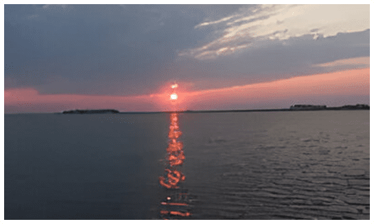 A sunset over the ocean with water in front of it.